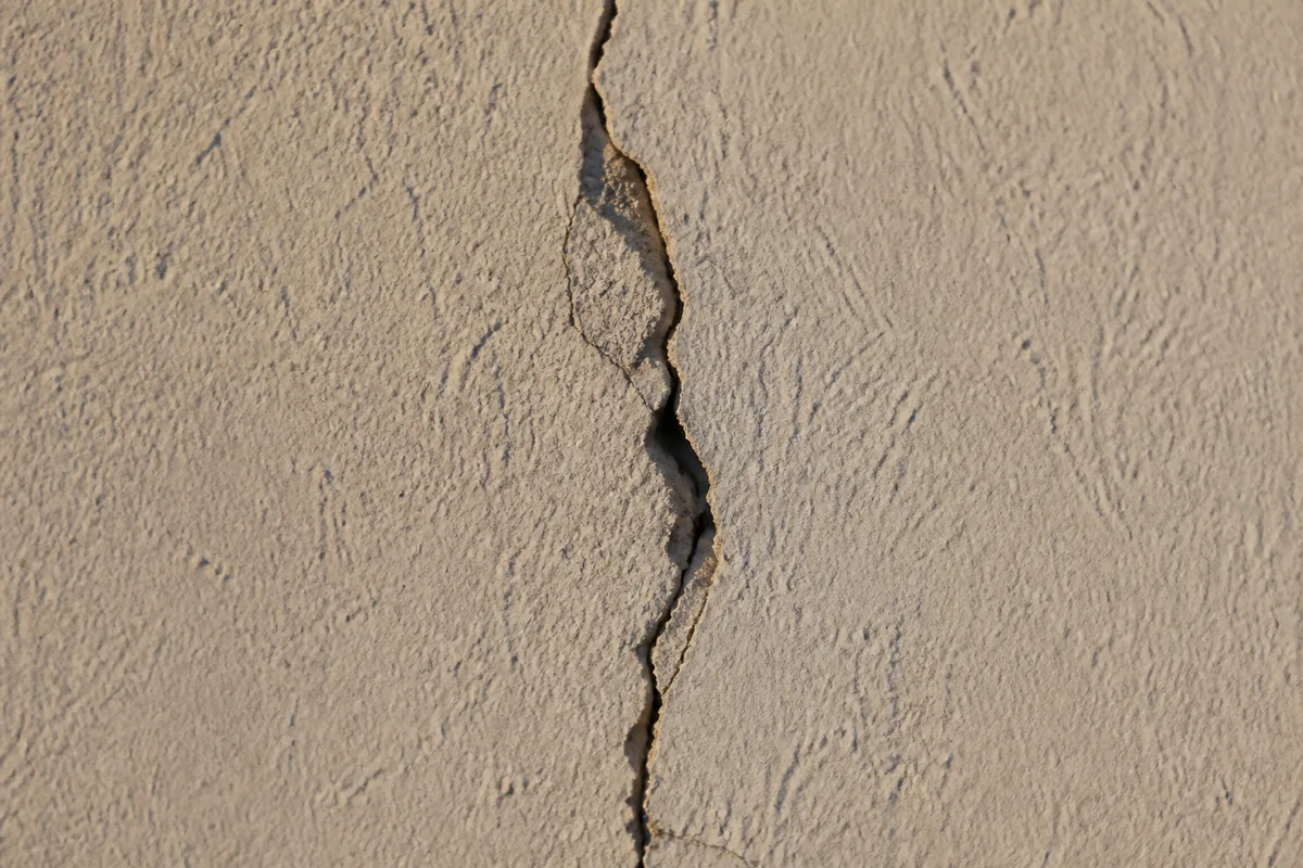 Fissure verticale sur un mur de façade en enduit clair, lumière rasante de fin de journée