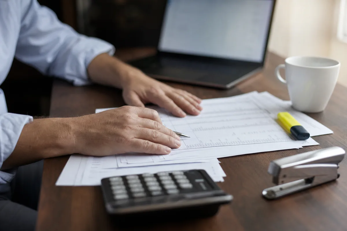 Dirigeant d&rsquo;entreprise étudiant des documents comptables dans un bureau français, visage hors champ