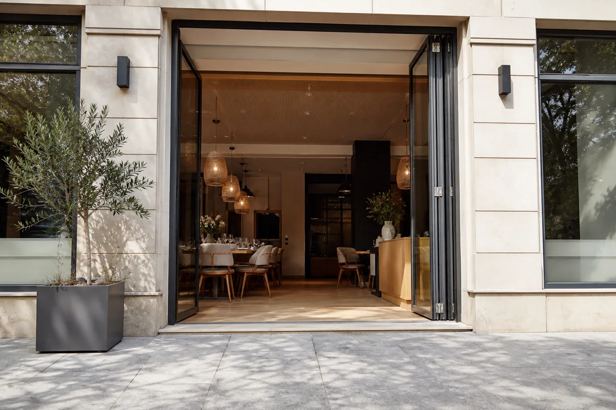 Entrée accessible d’un restaurant, rampe douce et porte vitrée grande ouverte sur une allée dégagée, façade en pierre claire