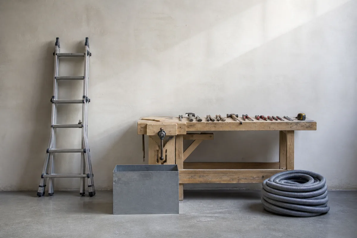 Atelier technique avec une échelle repliée contre un mur clair et des outils rangés sur un établi